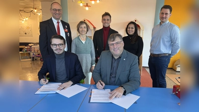 Dennis Behrendt und Stefan Löwl )rechts) unterzeichnen den Vertrag. Im Hintergrund: Bernhard Seidenath, Lisa Zimprich, Michael Schäfer, Dupinder Mohan und Dominik Ulbrich (von links). (Foto: BRK Dachau)