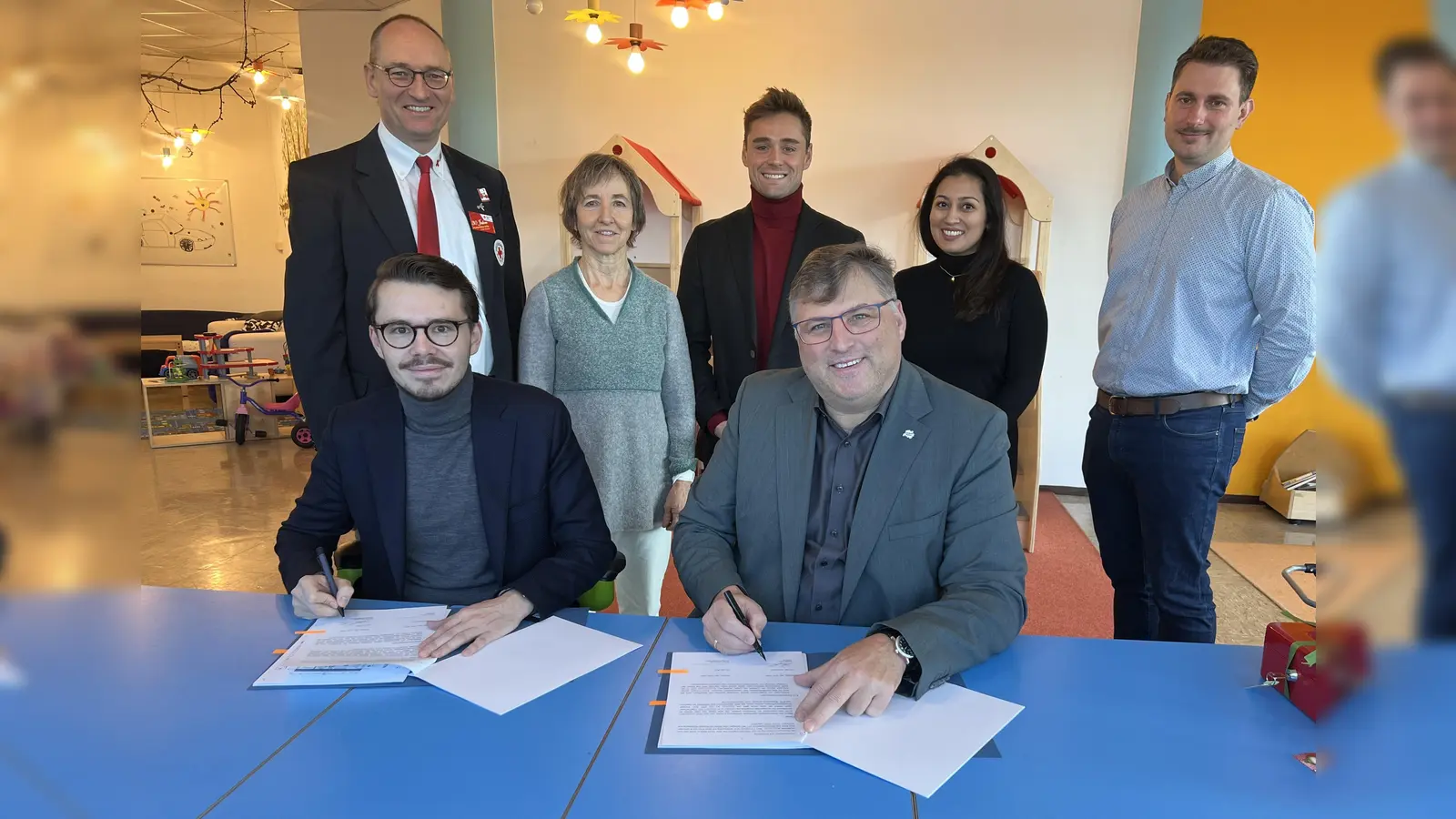 Dennis Behrendt und Stefan Löwl )rechts) unterzeichnen den Vertrag. Im Hintergrund: Bernhard Seidenath, Lisa Zimprich, Michael Schäfer, Dupinder Mohan und Dominik Ulbrich (von links). (Foto: BRK Dachau)