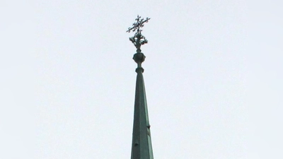 Eine schlanke Spitze mit einem Ornamentkreuz: Zu welcher Kirche gehört sie? (Foto: cr)