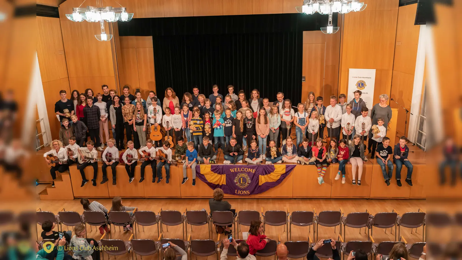 Die Preisträger mit ihren Lehrern und den Aschheimer Gitarrenkindern. In der Bildmitte hinten steht Guido Ruther, der die Veranstaltung moderierte. (Foto: Lionsclub Aschheim)