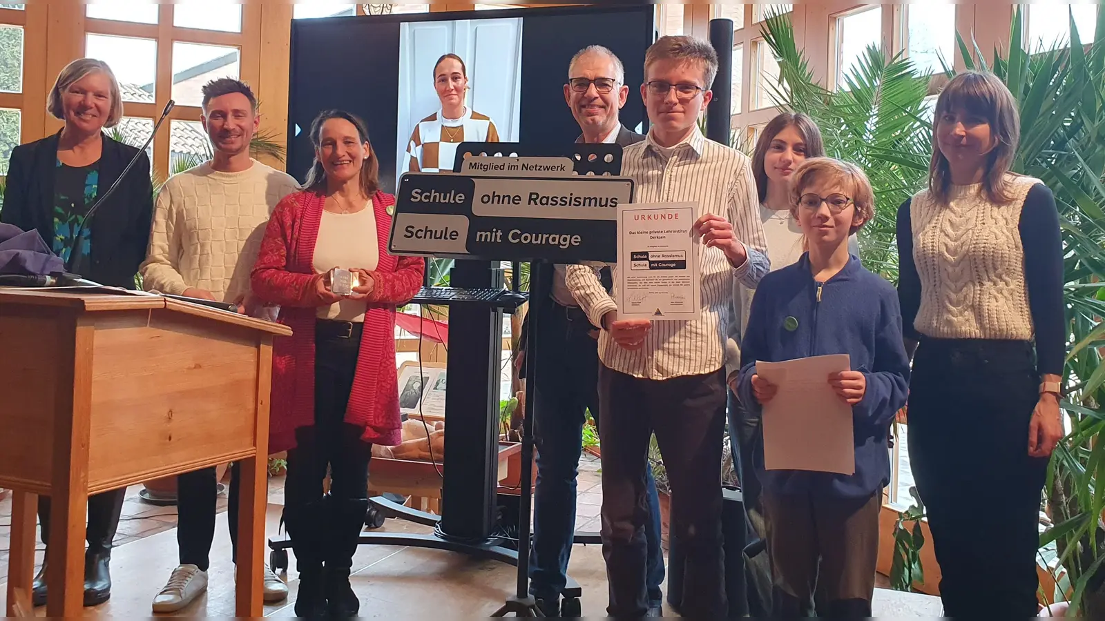 Freuen sich über die Plakette und Urkunde (von links): Schulleiterin Monika Aman, Regionalkoordinator Oberbayern Tobias Wolf, Lehrkraft Dr. Anne Stempel, Schülervater Ulrich Zehfuß, SMV-Mitglied Sebastian Heinke, SMV-Mitglied Leandra Schalm, SMV-Mitglied Leonard Pröll, Lehrkraft Tine Hohmann; im Hintergrund zu sehen Patin Sydney Lohmann. (Foto: Elisabeth Hiemer)