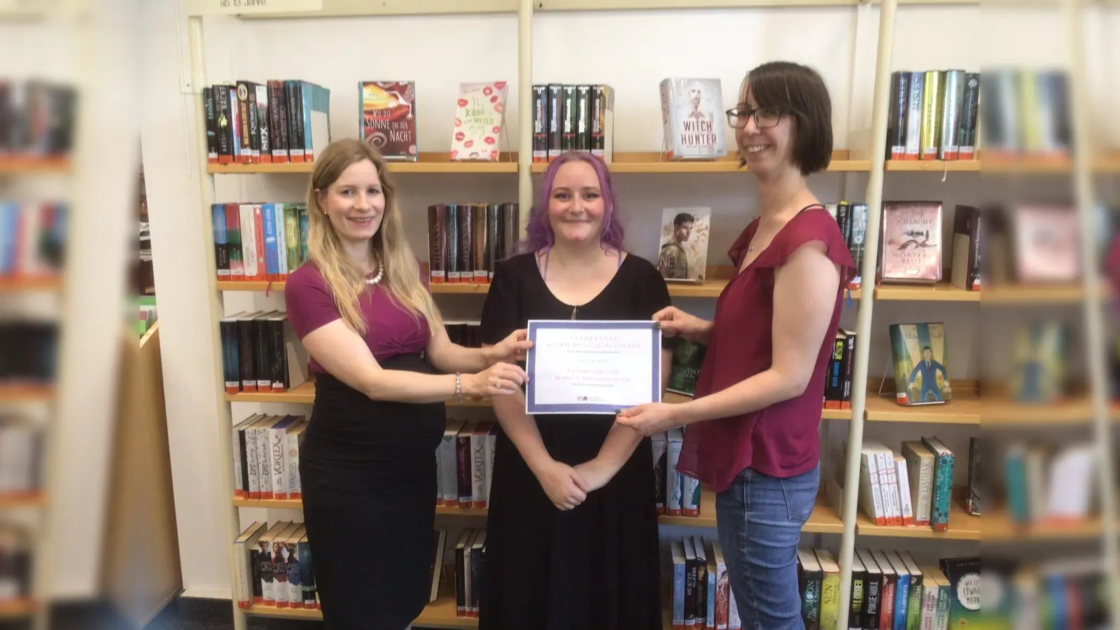 Büchereileiterin Ilona Obermeier (links), Auszubildende Eileen Selmeczi (Mitte) und Ausbilderin <br>Daniela Ponholzer (rechts) präsentieren die Urkunde als anerkannte Ausbildungsbibliothek. (Foto: Stadtbücherei Starnberg)