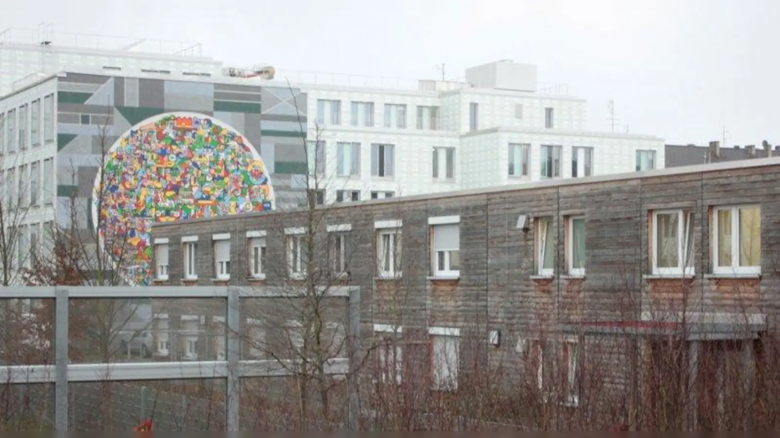 Zwischen Plinganserschule, Sozialbürgerhaus (2016 brachten Armin Kiss-Istok und Johannes Brechter ihr Fassadenbild „We Are All One” hier an, Hintergrund) und Bahn liegt die Gemeinschaftsunterkunft. An ihrer Stelle entsteht einmal das Mehrgenerationenhaus. (Foto: job)