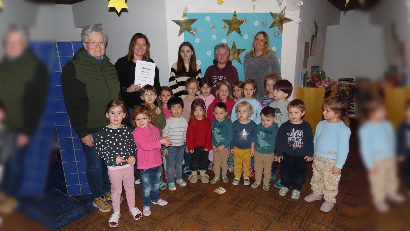 Anni Wachinger (li) überreicht der Leiterin des Kindergarten St. Barbara Bettina Huber und ihrem Team den Spendenscheck. Freudig und überrascht aufgenommen wurde es auch von einer Schar Kinder die sich gerne dem Fotografen stellten. (Foto: Georg Rittler)