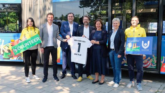 Neben zwei Volunteers freuten sich (v.l.) Dr. Felix Brych, Ingo Wortmann, Florian Kraus, Brgm. Verena Dietl und Silke Raml bei der Vorstellung der im EURO 2024-Design gebrandeten Fahrzeuge. Foto: R. Bösl